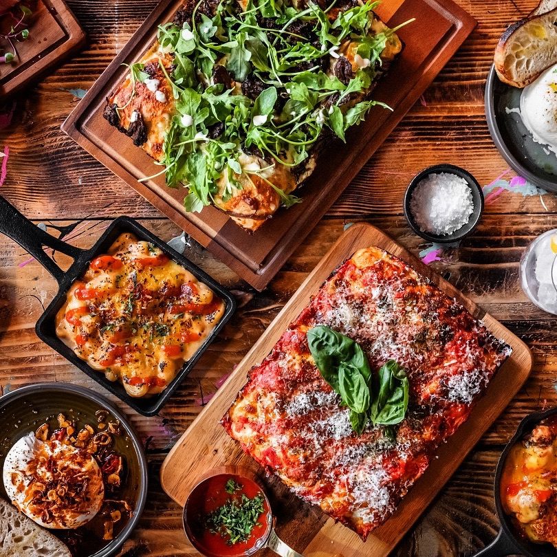 A spread of food from POP Kitchen including macaroni cheese and Detroit style pizza topped with basil leaves and rocket salad